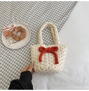 Detail view of a quilted cotton handbag with red bow accent on a checkered backdrop