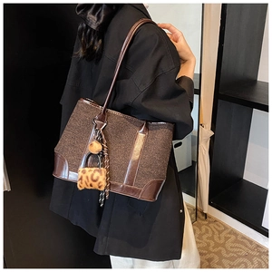 Detail of dark brown woven tote bag with leopard print charm and tassel on model