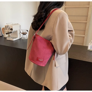 Detail of burgundy bucket bag with leather brand tag worn by model in urban setting