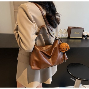 Detailed view of brown PU leather shoulder bag with plush dog charm and gold hardware