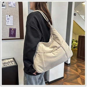 Detail of a large cream nylon dumpling bag with quilted texture and wide shoulder strap
