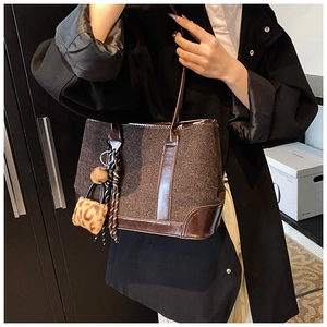 Close-up of brown tweed shoulder bag featuring glossy faux leather trim and leopard pom charm