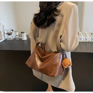 Detail of a brown pleated soft leather handbag with a cute teddy bear plush charm