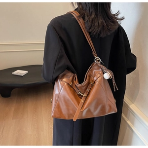 Detail of caramel brown PU leather shoulder bag with chic rivet straps and baseball charm