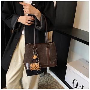 Close-up of brown tweed tote bag featuring faux leather trim and leopard plush charm