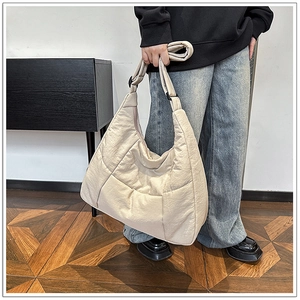 Detailed side view of beige quilted hobo bag with wide shoulder strap worn by model