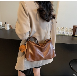 Detail of dark brown matte leather shoulder bag with vintage metal lock and plush charm