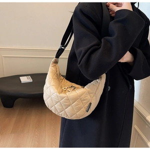 Detail of light beige quilted crescent bag with adjustable black shoulder strap and zipper