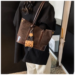 Detail of wool texture and leather trim on deep brown tote bag with plush charm
