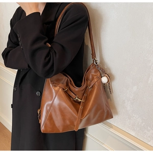Detail of dark brown PU leather shoulder bag featuring a baseball pendant and adjustable strap