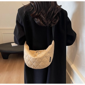Close-up of beige quilted puffy crossbody bag with detailed stitching and black logo label