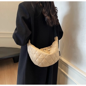 Detail of beige quilted crescent crossbody bag with grid stitching on black wool coat