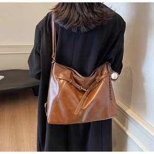 Detailed view of brown retro leather tote bag featuring baseball pendant and metal buckle