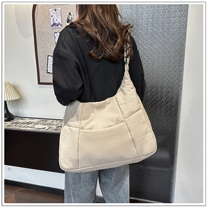 Detail of a large beige quilted crossbody dumpling bag worn in a casual home setting