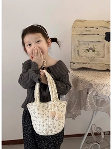 Détail du sac à main en coton fleuri avec dentelle et pompons roses sur un modèle