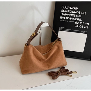 Brown suede hobo bag with adjustable shoulder strap and gold zipper on marble surface