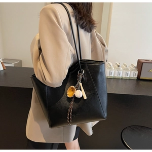 Gros plan d'un sac cabas en similicuir noir avec pendentif baseball porté par un mannequin