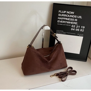 Dark brown suede hobo bag with gold hardware and adjustable strap on a marble surface