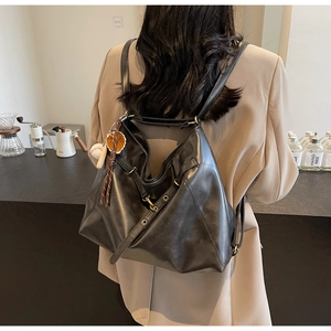 Detail of soft black PU leather backpack with tassel and baseball charm in cafe setting