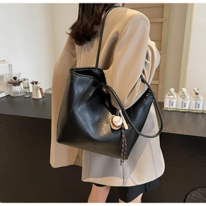 Détail d'un sac cabas en cuir PU noir avec breloque de baseball porté par un modèle