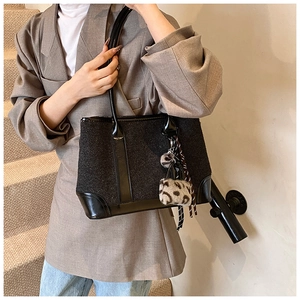 Close-up of black tweed tote bag with smooth leather handles and leopard print charm