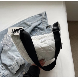 Quilted white half-moon crossbody bag with wide black strap on denim jacket background