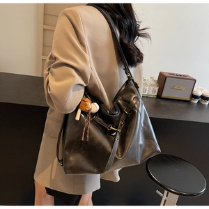Detail of a large black PU leather tote bag with baseball charm and metal buckle accents