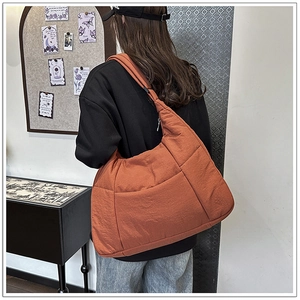 Detail of a large orange crescent shoulder bag featuring a soft quilted canvas texture