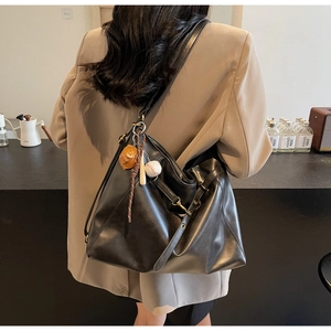 Close-up of black PU leather tote bag with baseball charm on model in beige blazer