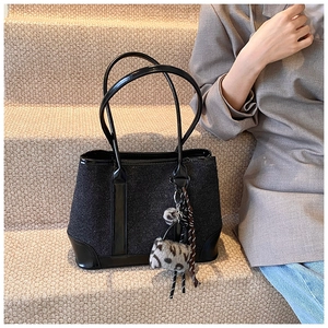 Detail of black tweed tote bag featuring glossy patent leather straps and pompom charm