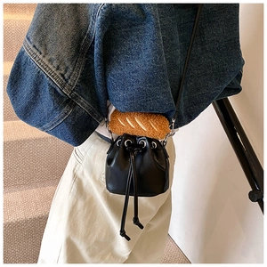 Close-up of mini black PU leather bucket bag with brown plush bread charm decoration
