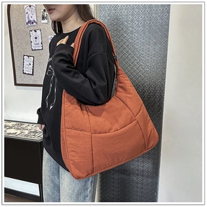 Detailed side view of caramel orange quilted nylon crossbody bag with wide strap on model