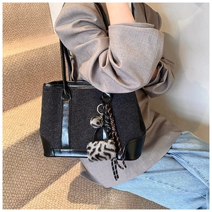 Detail of black tweed tote bag with leather trim and decorative fur ball keychain charm