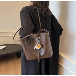 Détail d'un sac cabas marron foncé en similicuir avec breloques de baseball et texture lisse
