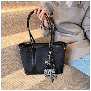 Close-up of a grey wool tote bag with black leather straps and leopard fur charm