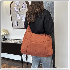 Rear view of a large orange quilted dumpling bag worn by a model in a cozy interior