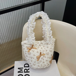 Borsa a tracolla trapuntata a fiori con manici in pizzo e fiocchi su sedia color crema