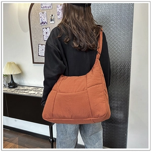 Detail view of orange quilted crossbody bag with padded strap on model for daily use