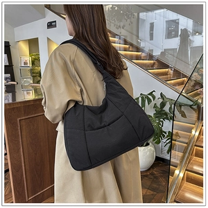 Detailed view of the large black quilted dumpling bag worn by a model in a modern room