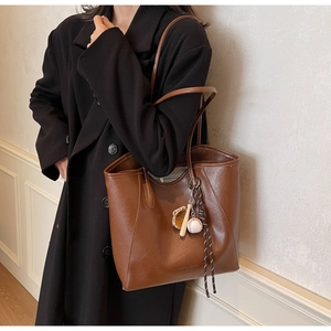 Détail d'un sac cabas en cuir PU marron avec pendentifs de baseball et texture vintage