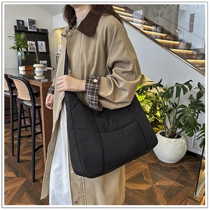 Detailed view of black quilted puffer tote bag styled with a casual trench coat