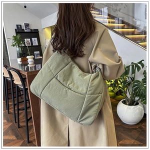 Detail view of a large green quilted tote bag showing its texture and casual drape on shoulder
