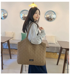 Close-up of brown quilted tote bag with heart patterns and brand logo detail