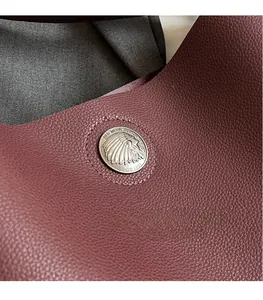 Close-up of vintage silver coin hardware on textured burgundy lychee grain leather bag