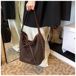 Detail showing the woven texture and leather brand label on a brown bucket shoulder bag