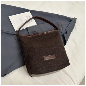 Detailed view of dark brown textured fabric bucket bag with leather trim and OUSHEYA logo