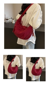 Detail of burgundy crescent crossbody bag showing textured nylon and woven zipper pull
