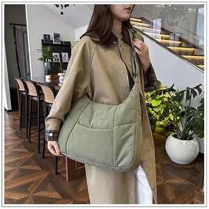 Sage green quilted dumpling bag worn cross-body style over a beige trench coat