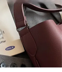 Detail of burgundy lychee grain leather bag with dark metallic buckle and fine stitching