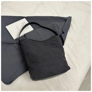 Detail view of dark grey canvas bucket bag with black leather straps on grey suit jacket